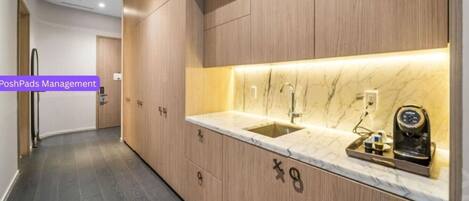 A modern kitchen with wooden cabinetry, a marble countertop, and a built-in coffee machine.