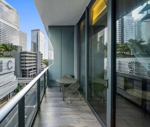 A balcony with a table and chairs, a glass door, and a view of city buildings.