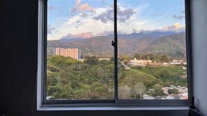 A room with a large window offering a view of a mountainous landscape, buildings, and greenery. - Exotic family getaway (Armenia)