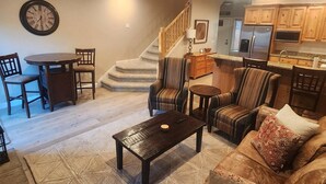 A living room with a dining table, chairs, a sofa, and a coffee table. There is a staircase leading to an upper level. - Condo Near Snowbasin, 2/2 (Huntsville)