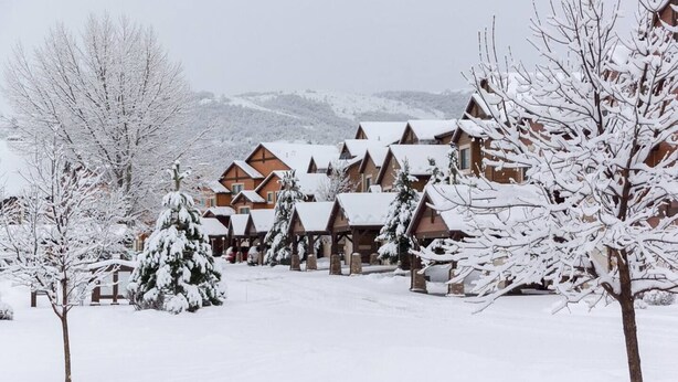 A snow-covered lodge with multiple wooden cabins, a central building, and snow-laden trees. - Condo Near Snowbasin, 2/2 (Huntsville)