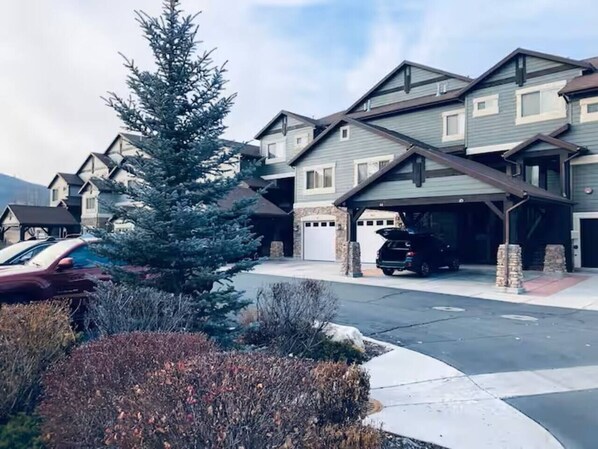 A residential area with multi-story houses, a parking garage, and a large evergreen tree.