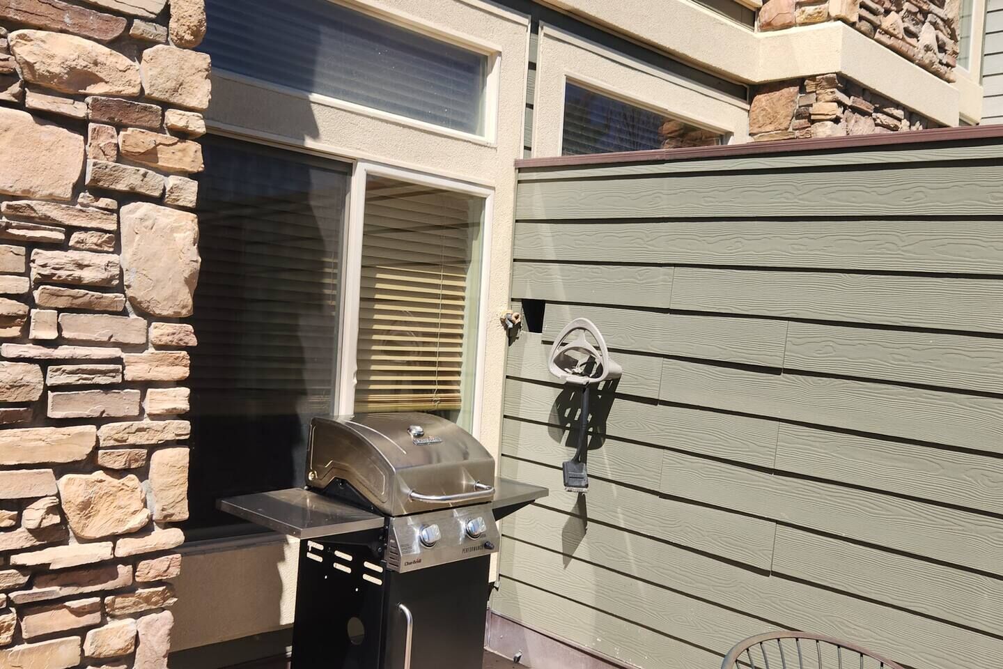 Una griglia per barbecue fissata a un muro in pietra, con una finestra e persiane sullo sfondo.