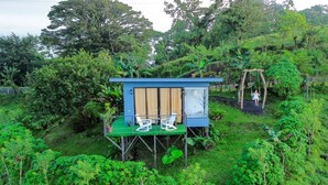 A small, elevated wooden structure with a green roof, two white chairs, and a table, surrounded by lush greenery. - Eco Sol, Volcano and Lake Panoramic View, with hammock. (La Fortuna)