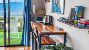 A room with a wooden table, a kettle, a remote control, and a view of mountains through a glass door. - Eco Sol, Volcano and Lake Panoramic View, with hammock. (La Fortuna)