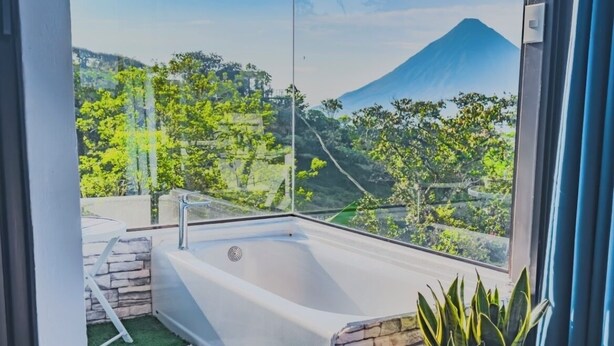 A modern bathroom with a bathtub, a potted plant, and a view of a mountainous landscape. - Eco Sol, Volcano and Lake Panoramic View, with hammock. (La Fortuna)