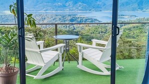 A balcony with two rocking chairs and a small table, overlooking a mountainous landscape with a lake. - Eco Sol, Volcano and Lake Panoramic View, with hammock. (La Fortuna)