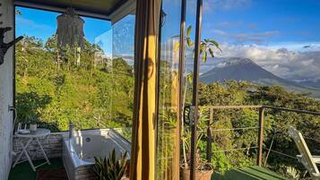 A balcony with a view of a volcano, a jacuzzi, and potted plants.