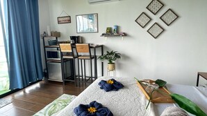 A cozy room with a bed, a desk, and a chair. There is a window with blue curtains, a wall-mounted air conditioner, and decorative wall art. - Eco Sol, Volcano and Lake Panoramic View, with hammock. (La Fortuna)