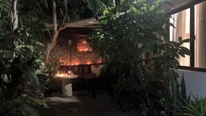 An outdoor seating area with stone walls and a fire feature, surrounded by dense foliage. - Imani’s home (Mombasa)