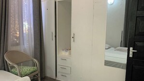 A bedroom with a bed, a chair, a wardrobe, and a mirror. - Imani’s home (Mombasa)