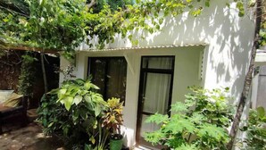 A small, white building with a door and windows, surrounded by lush greenery and plants. - Imani’s home (Mombasa)
