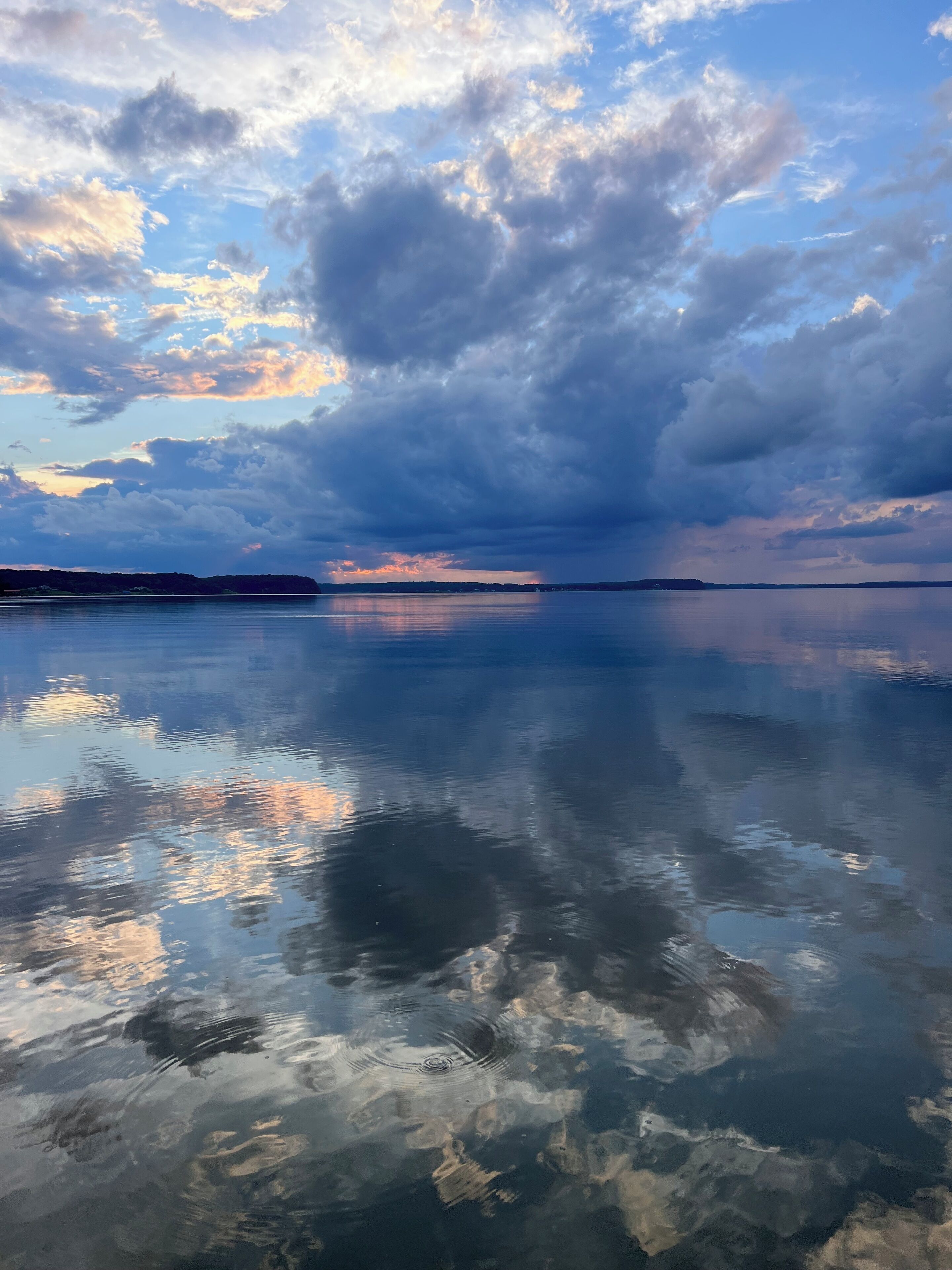 Un lac paisible où se reflètent les nuages et où l’on aperçoit une rive lointaine.