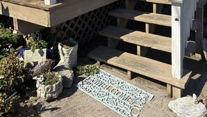 A wooden deck with a white railing, a stone planter with a face, and a welcome mat. - The ShellHunter getaway at Fairview Beach. The perfect place to disconnect. (King George)