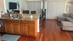 A modern kitchen with granite countertops, wooden cabinets, and a built-in island. There is a dining area with a table and chairs, a fireplace, and a large window with blinds. - The ShellHunter getaway at Fairview Beach. The perfect place to disconnect. (King George)