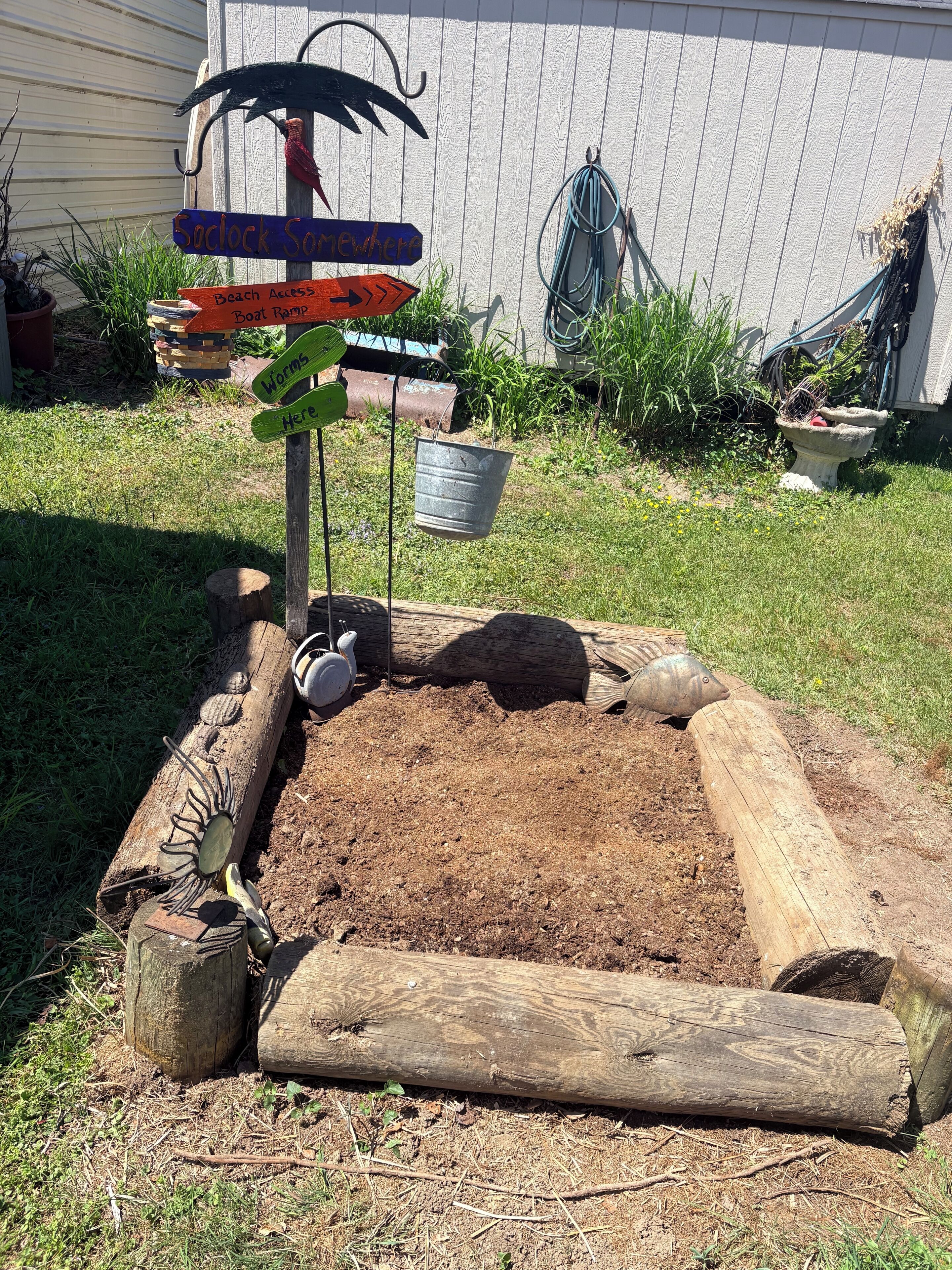 A garden bed with a wooden border, a metal bucket, and a signpost with directional arrows.