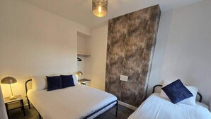Une chambre d’hôtel avec deux lits, chacun agrémenté de draps blancs et d’oreillers foncés, une petite table de chevet avec une lampe et un mur à motifs.
