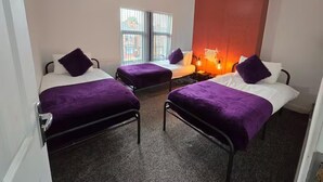 A room with two beds, each with a purple blanket and pillow, a small table, and a window with blinds. - 4 Bed-sleeps 9-private Garden-free Parking (Birmingham)
