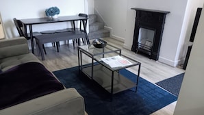A modern living room with a glass coffee table, grey sofa, and a fireplace. - 4 Bed-sleeps 9-private Garden-free Parking (Birmingham)