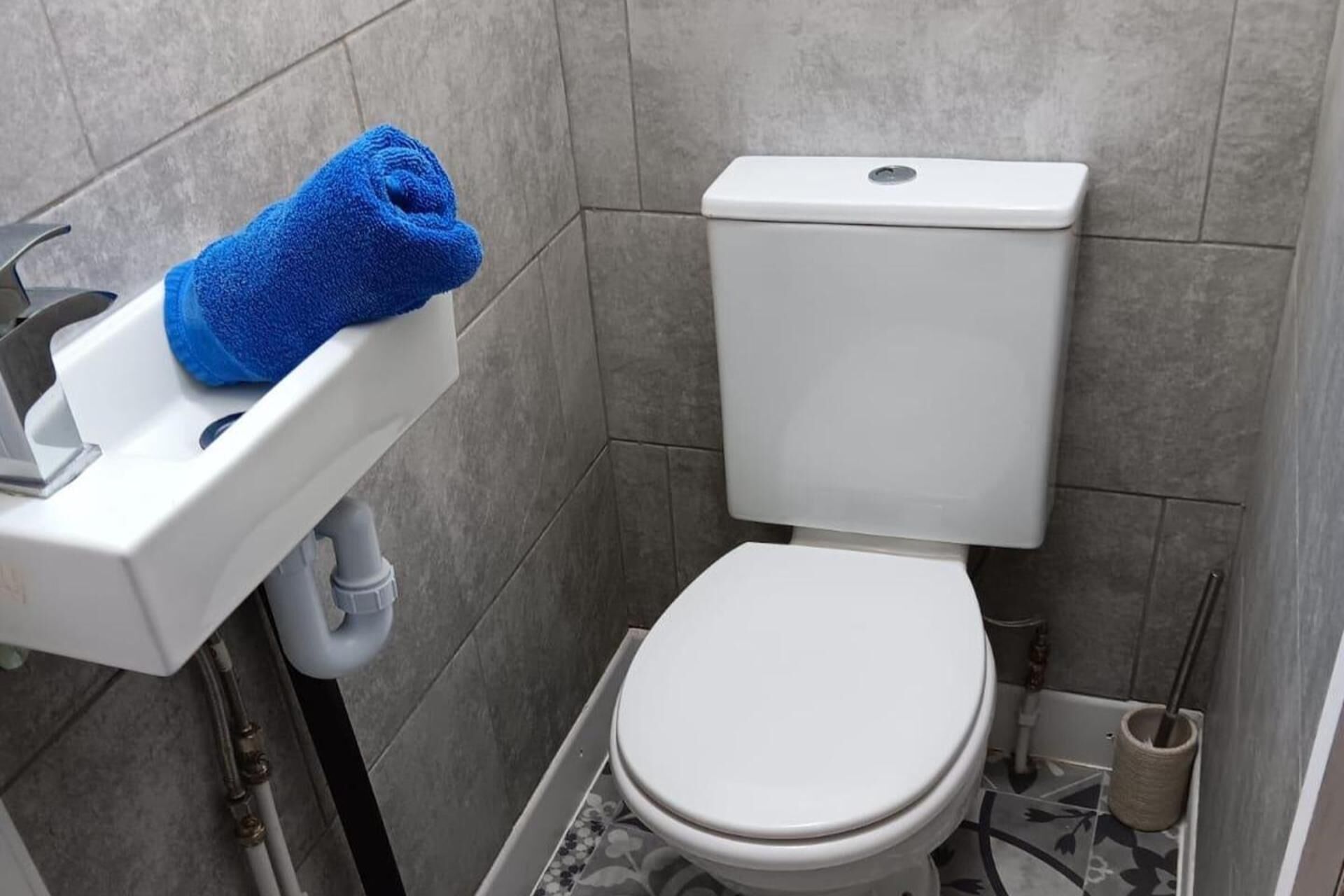 A bathroom with a white toilet, a sink with a blue towel, and a toilet brush.