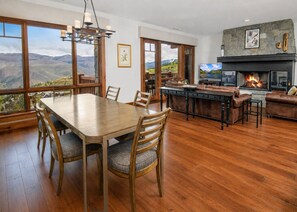 Amplia sala de estar con una gran mesa de comedor, asientos cómodos, chimenea y ventanas amplias que ofrecen vistas a la montaña.