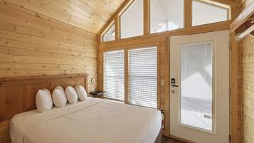 Ein Schlafzimmer mit Holzwandverkleidung, einem Bett, einem Nachttisch und einer Tür mit Fenster.