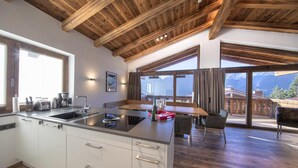 A modern kitchen with a central island, wooden ceiling beams, and large windows offering mountain views. - Luxury Chalet With Ski Access (Neukirchen am Grossvenediger)