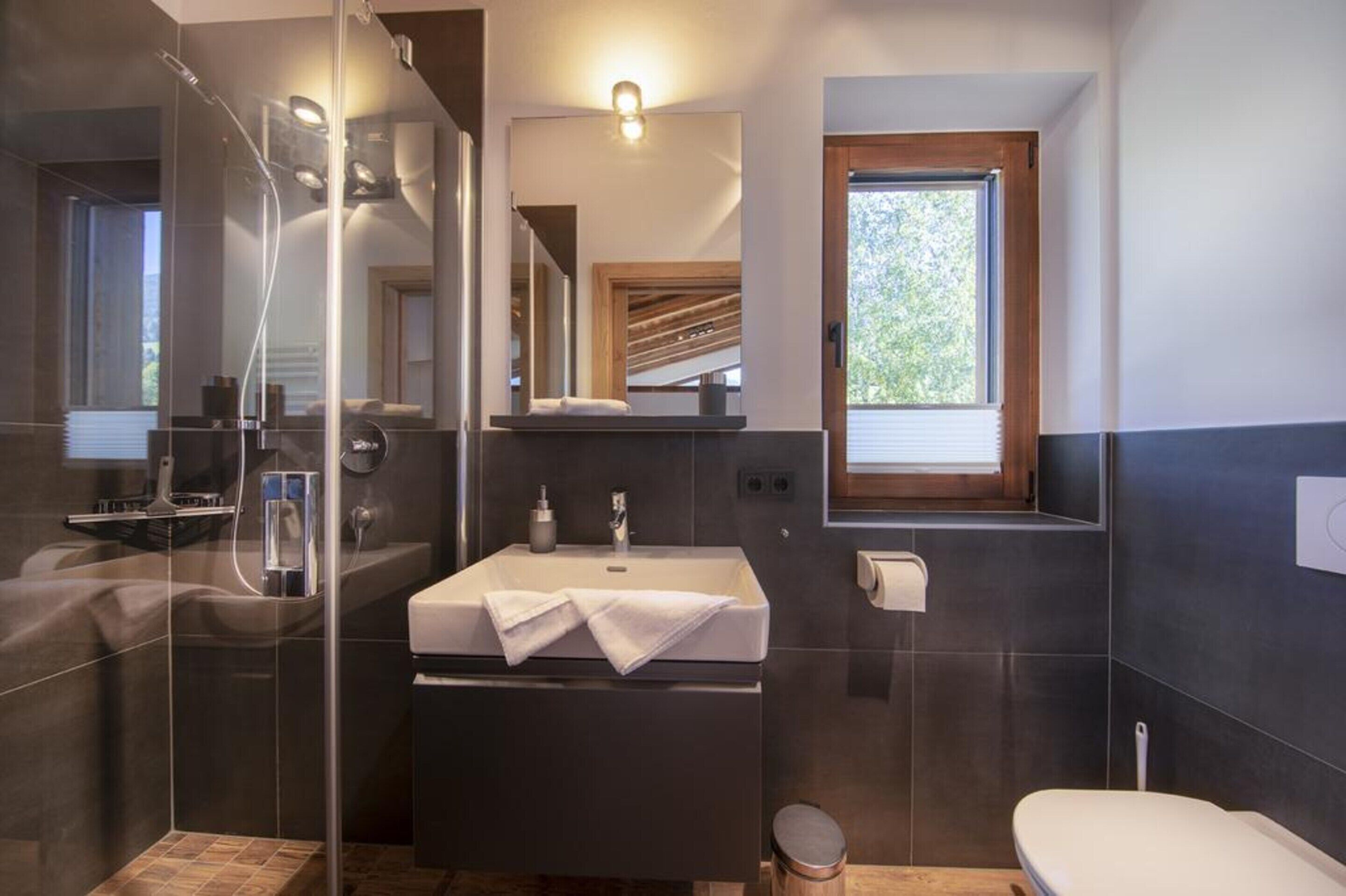A modern bathroom with a glass-enclosed shower, a large sink with a towel, and a window providing natural light.