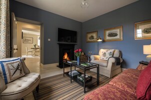 Una sala de estar con chimenea, un sofá, una mesa de centro con libros y cuadros en la pared.
