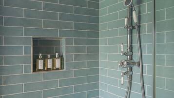 A bathroom with teal-tiled walls, a shower with a handheld showerhead, and a shelf with three bottles.