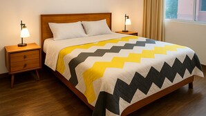A neatly made bed with a geometric patterned bedspread, two bedside tables with lamps, and a window with curtains. - 2 bedroom apartment in cuenca (Cuenca)