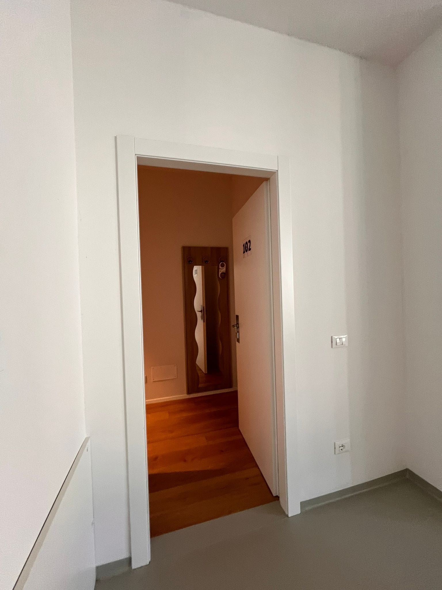 A hallway with a wooden staircase leading to a room with a door marked '102'.