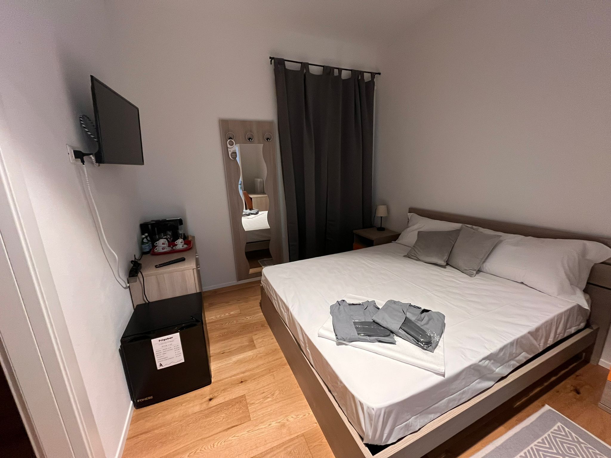 A hotel room with a bed, a desk, a TV mounted on the wall, and a bathroom visible through a mirror.
