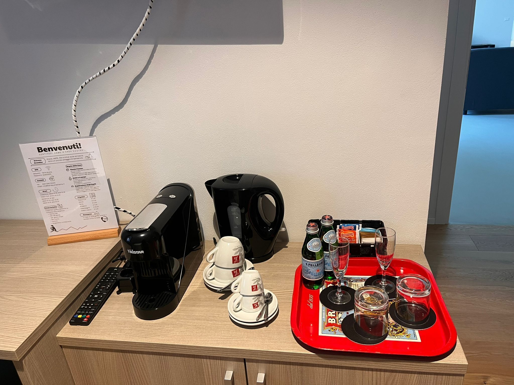 A coffee station with a coffee maker, a kettle, and a tray with cups, glasses, and condiments.
