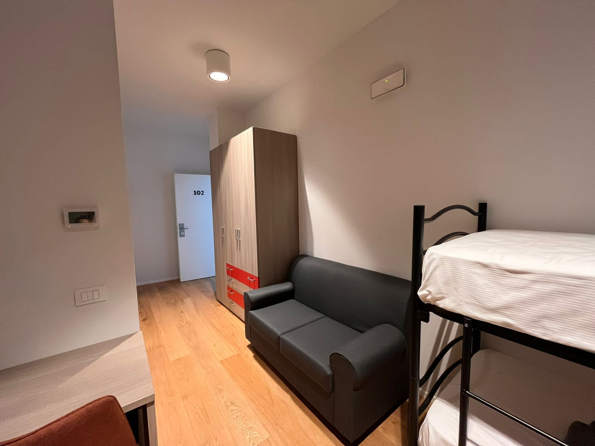 Habitación pequeña con literas, sofá, armario y un escritorio.