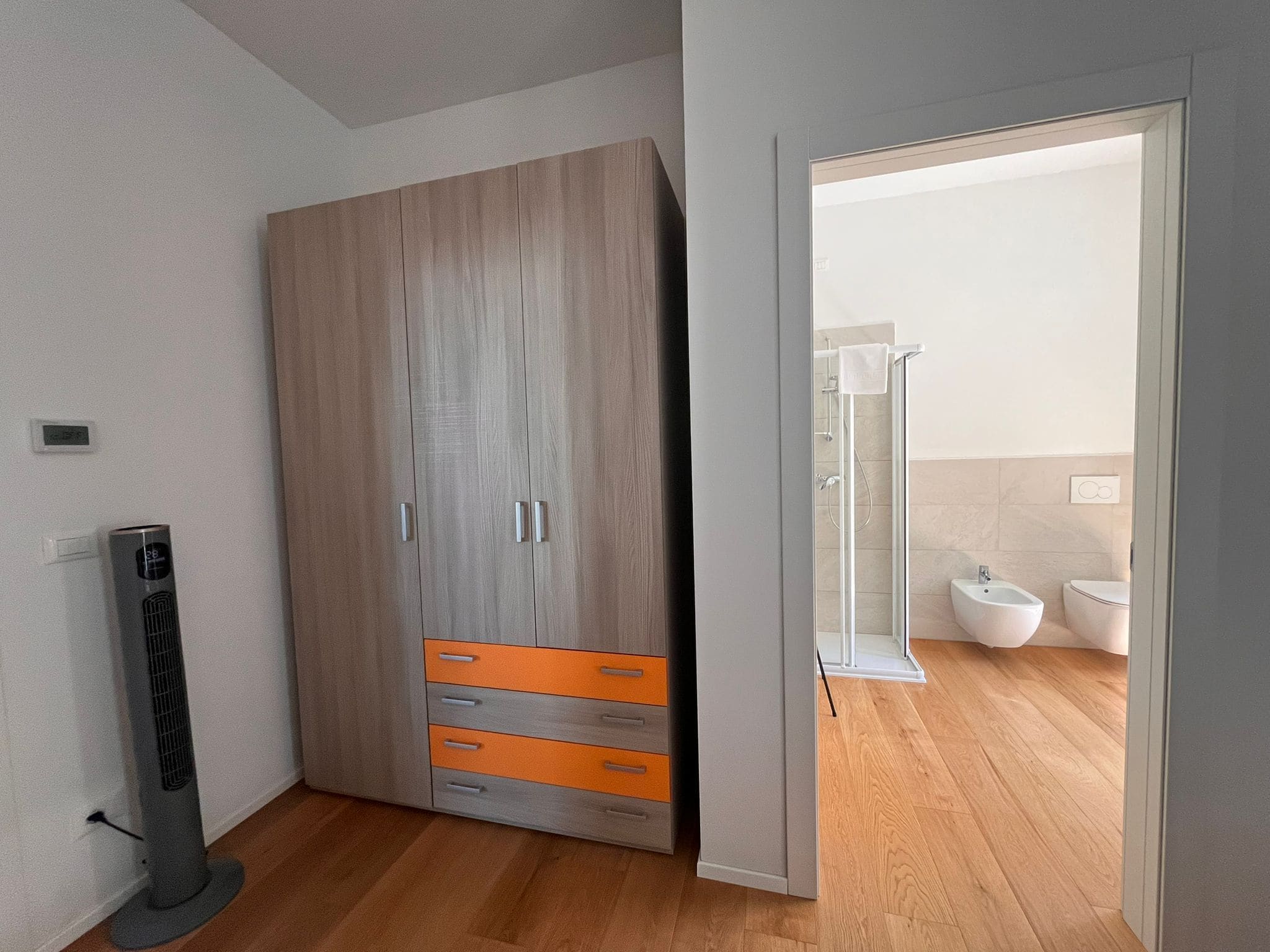 A modern bedroom with a wardrobe, a standing heater, and a view into the bathroom.