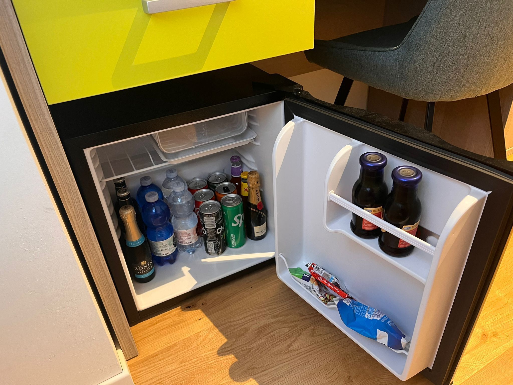 A compact refrigerator with multiple shelves, containing various beverages and snacks.