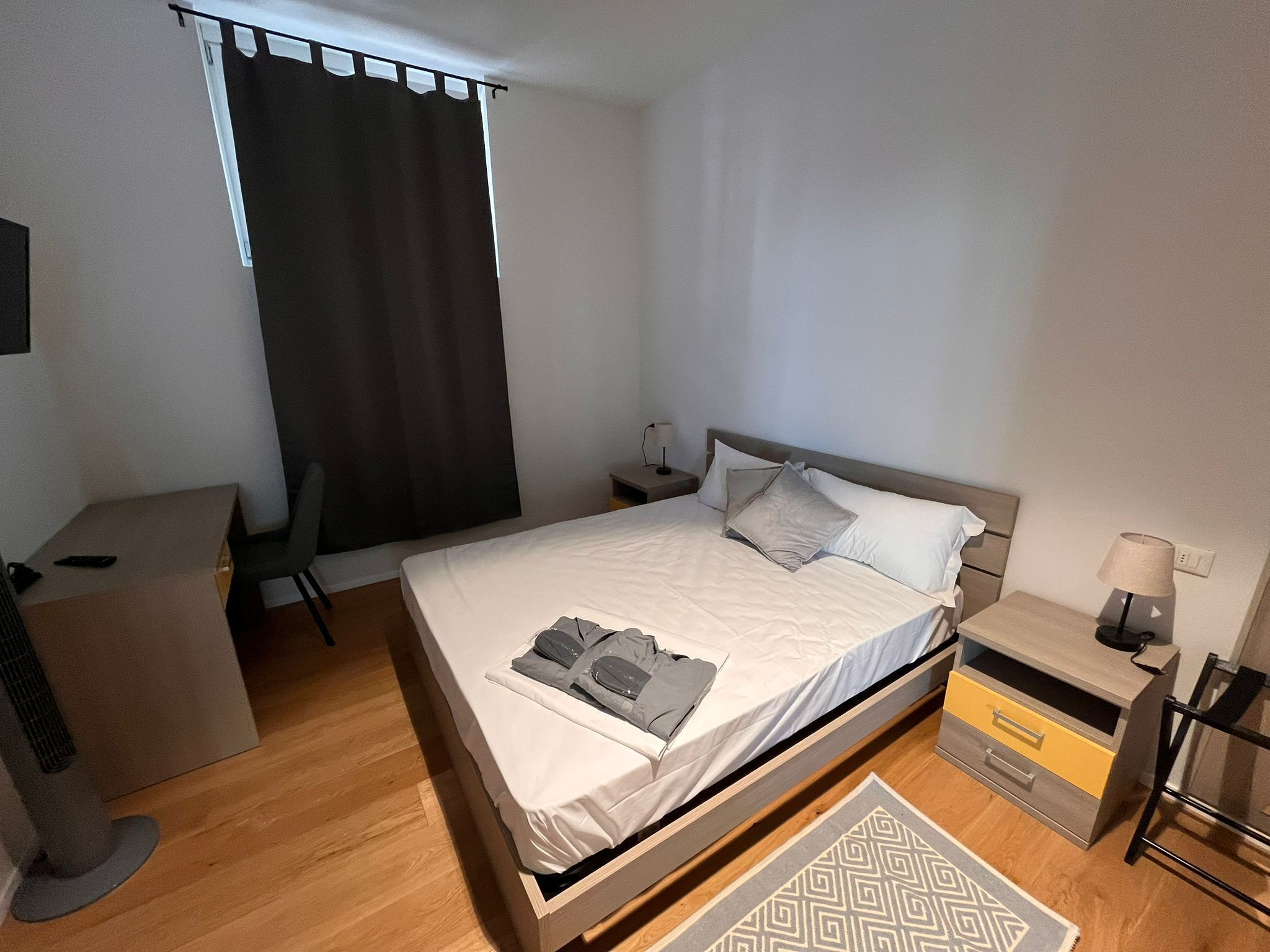 A neatly arranged hotel room with a single bed, bedside tables, a desk, and a chair.