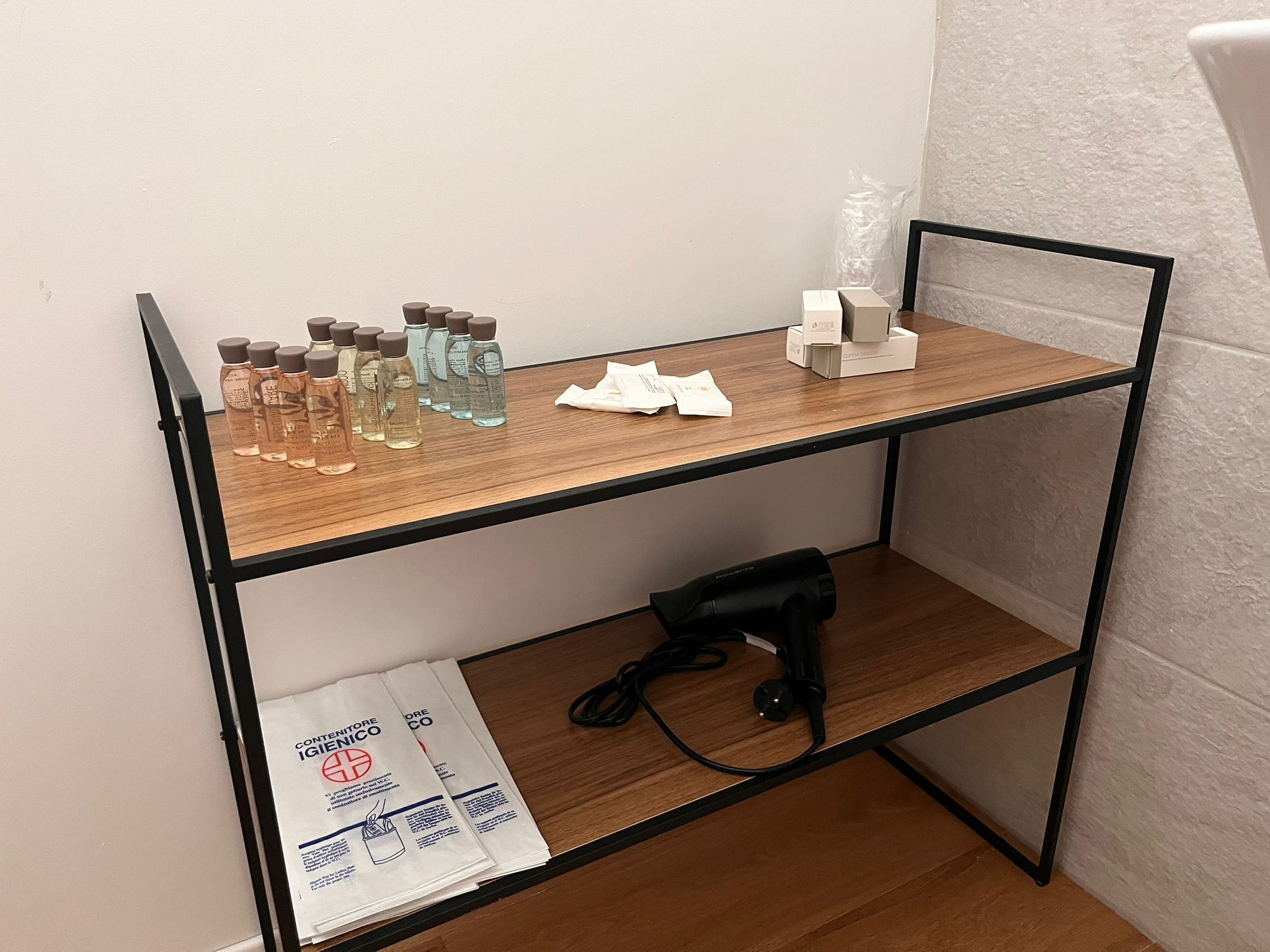 Una estantería de madera con varios objetos, entre ellos botellas, una pequeña caja blanca y un dispositivo negro.
