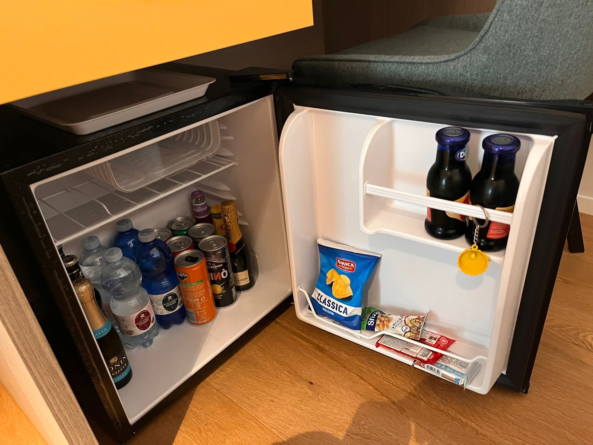 Un refrigerador compacto lleno de bebidas, aperitivos y salsas.