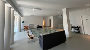 A spacious living area with a glass-top coffee table, a sofa, and a chair. There is a radiator, a sewing machine, and a door labeled "101". - Terra Buona Rooms (Traona)