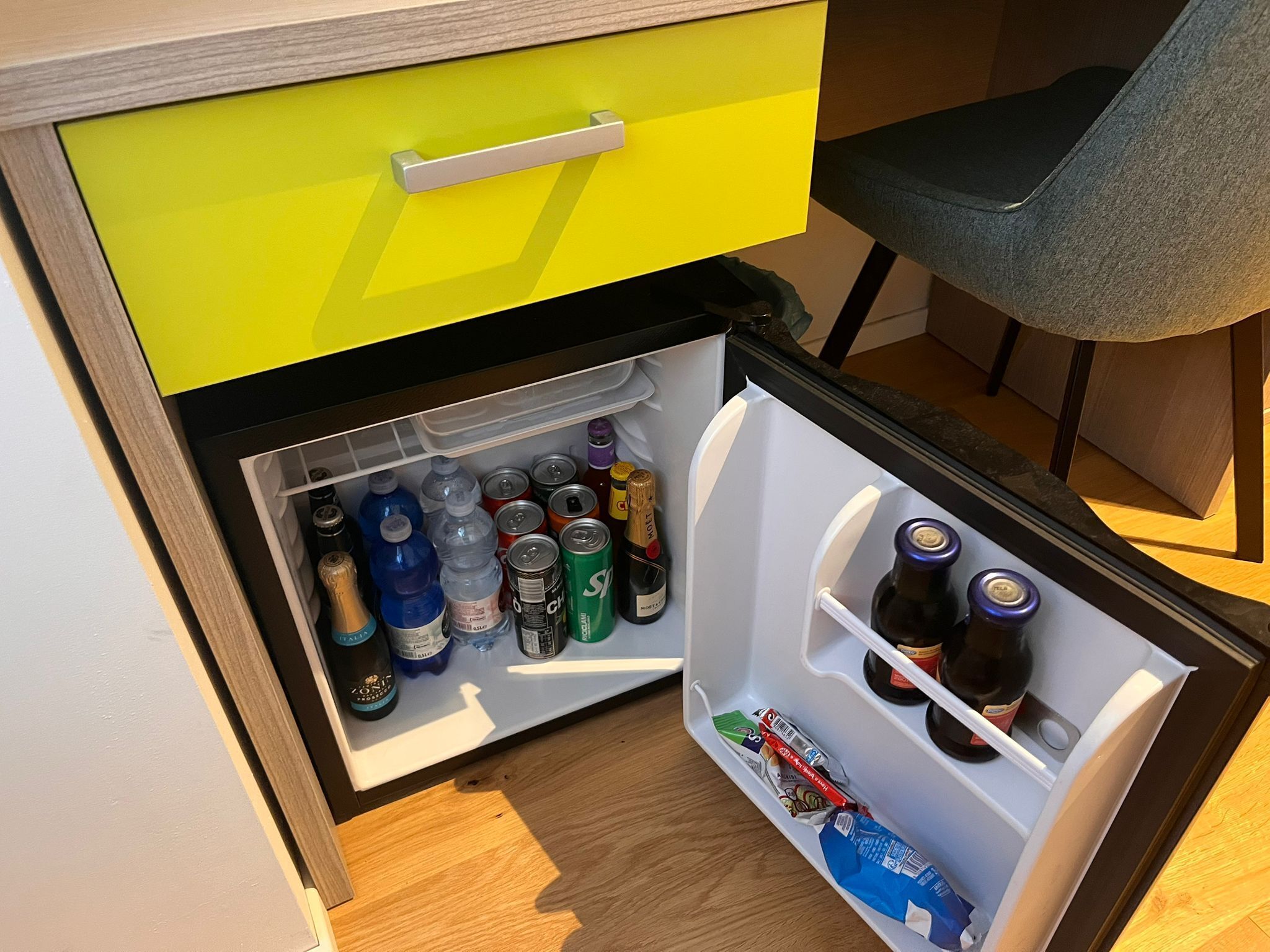 A compact refrigerator with a yellow handle drawer, containing various beverages and snacks.