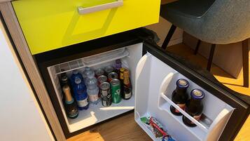 A compact refrigerator with a yellow handle drawer, containing various beverages and snacks.