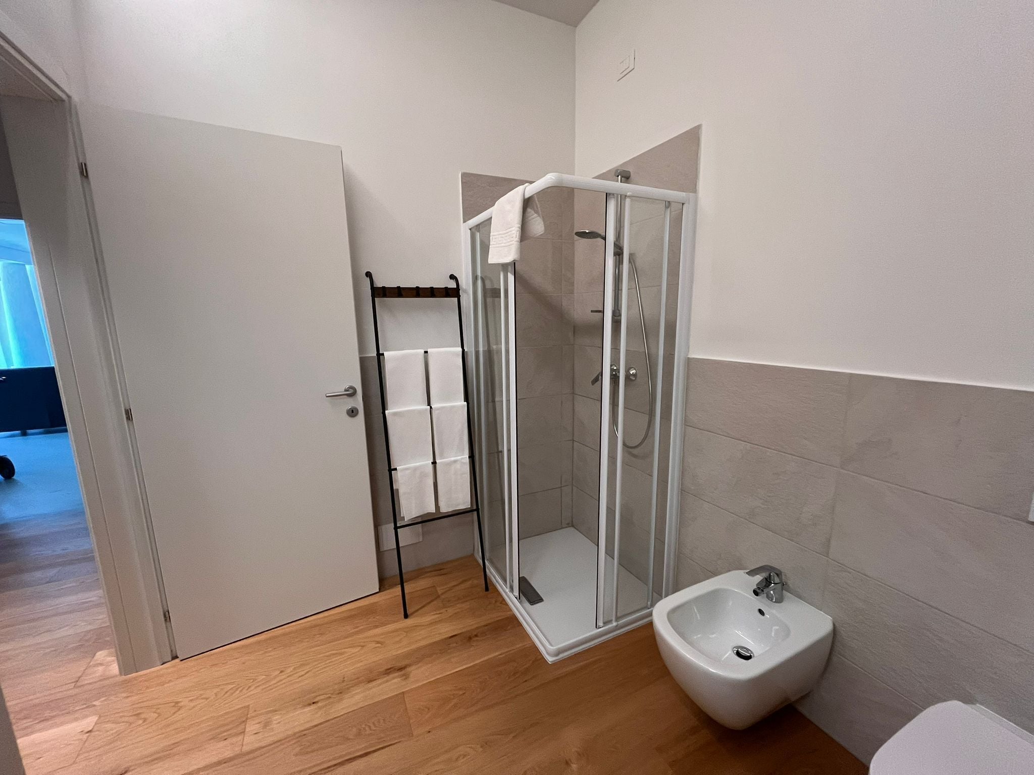 A modern bathroom with a glass-enclosed shower, a white sink, and a wooden floor.