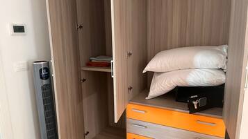 A bedroom with a bed, a heater, and a wardrobe with orange drawers.
