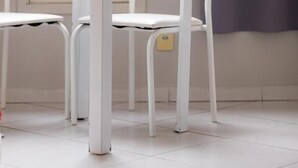 Een witte tafel met glazen blad en twee witte stoelen in een kamer met witte vloer en een raam met gordijn.