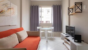Een moderne woonkamer met een bank, een televisie, een tafel met stoelen en een raam met gordijnen.
