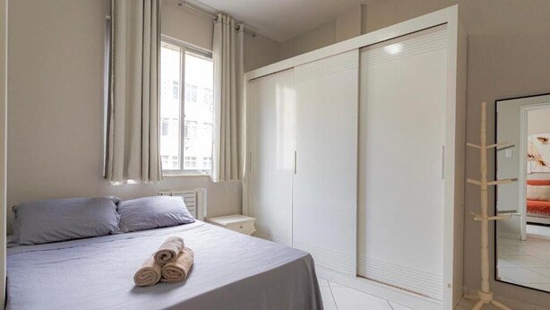 Een slaapkamer met een bed, een kledingkast, een nachtkastje en een raam met gordijnen.