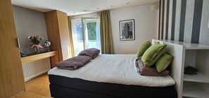 Una camera da letto con un letto, un comodino, uno specchio, una finestra e vista sul verde.