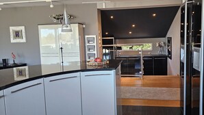A modern kitchen with a central island, a dining area with a glass partition, and a view of the outdoors.